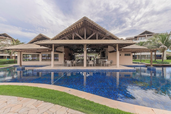 A hotel with a large outdoor pool, covered patio area, and multiple dining options.