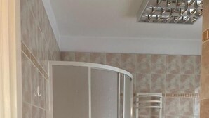 Um chuveiro com porta de vidro fosco, um porta-toalhas branco e paredes com azulejos bege.