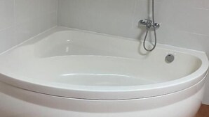 Uma banheira de canto com chuveiro, azulejos brancos nas paredes e pisos de azulejo marrom.