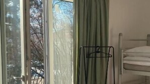 Quarto com porta de vidro deslizante que dá para uma varanda, uma cama beliche e um suporte de metal.