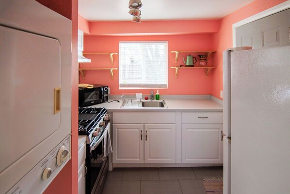 Pieni, käytännöllinen keittiö, jossa on valkoiset kaapit, liesi, mikroaaltouuni ja pesuallas.