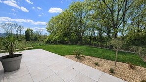 A patio area with a tiled floor, surrounded by a well-maintained lawn and trees. - New Home in Gulf of Morbihan & Vannes, Mahelia (Le Hézo)