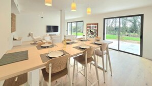 A modern dining area with a long table, chairs, and pendant lights. - New Home in Gulf of Morbihan & Vannes, Mahelia (Le Hézo)