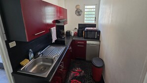 Ett kompakt kök med röda skåp, en diskho i rostfritt stål, en mikrovågsugn och en diskmaskin.