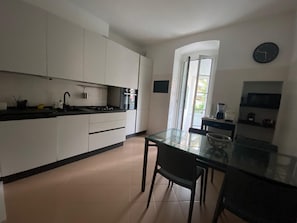 A modern kitchen with white cabinets, a black countertop, and a glass dining table. - Câ Giâna apartment 5 minutes from the beaches (Lavagna)