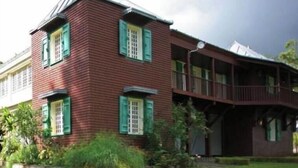 Ein zweistöckiges Gebäude mit roter Fassade und grünen Fensterläden, umgeben von einer gepflegten Rasenfläche.
