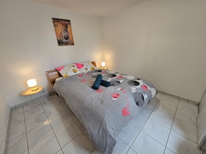 Un dormitorio con una cama, dos lámparas de noche, un cuadro en la pared y suelo de baldosas.