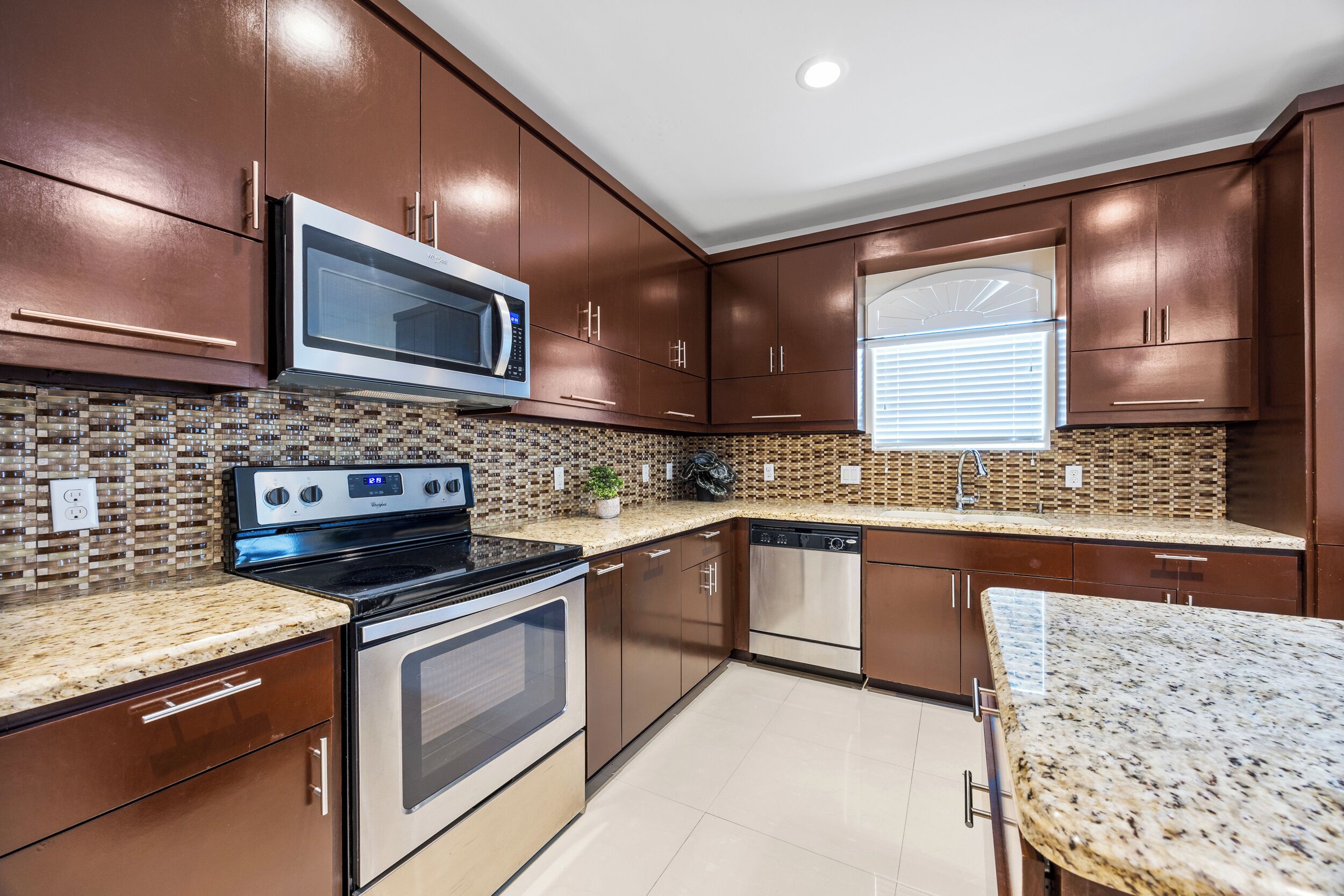A modern kitchen with dark brown cabinets, stainless steel appliances, and a tiled backsplash.