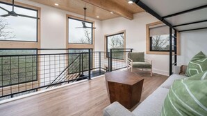 A modern interior with a wooden ceiling, large windows, a staircase, and a sofa with green cushions. - The Sun at In the Trees Luxury Resort🌳, Mountaintop, Hot Tub, Fireplace, Full Kitchen (Hot Springs National Park)