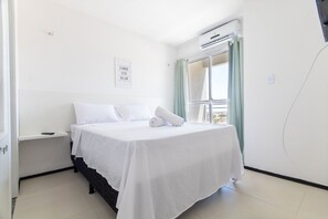 A clean, white hotel room with a bed, a nightstand, a wall-mounted air conditioner, and a window with curtains. - Exclusive Duplex at Beach Townhouse IV by Carpediem (Aquiraz)