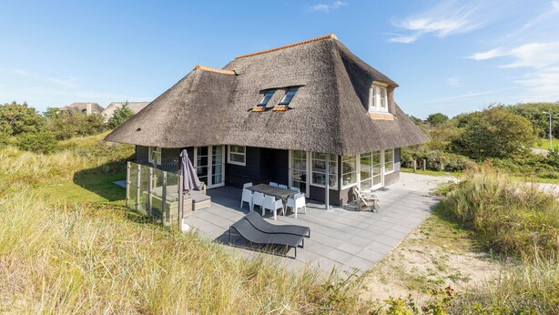Una casa con techo de paja, un patio con mobiliario exterior y vistas del paisaje circundante.