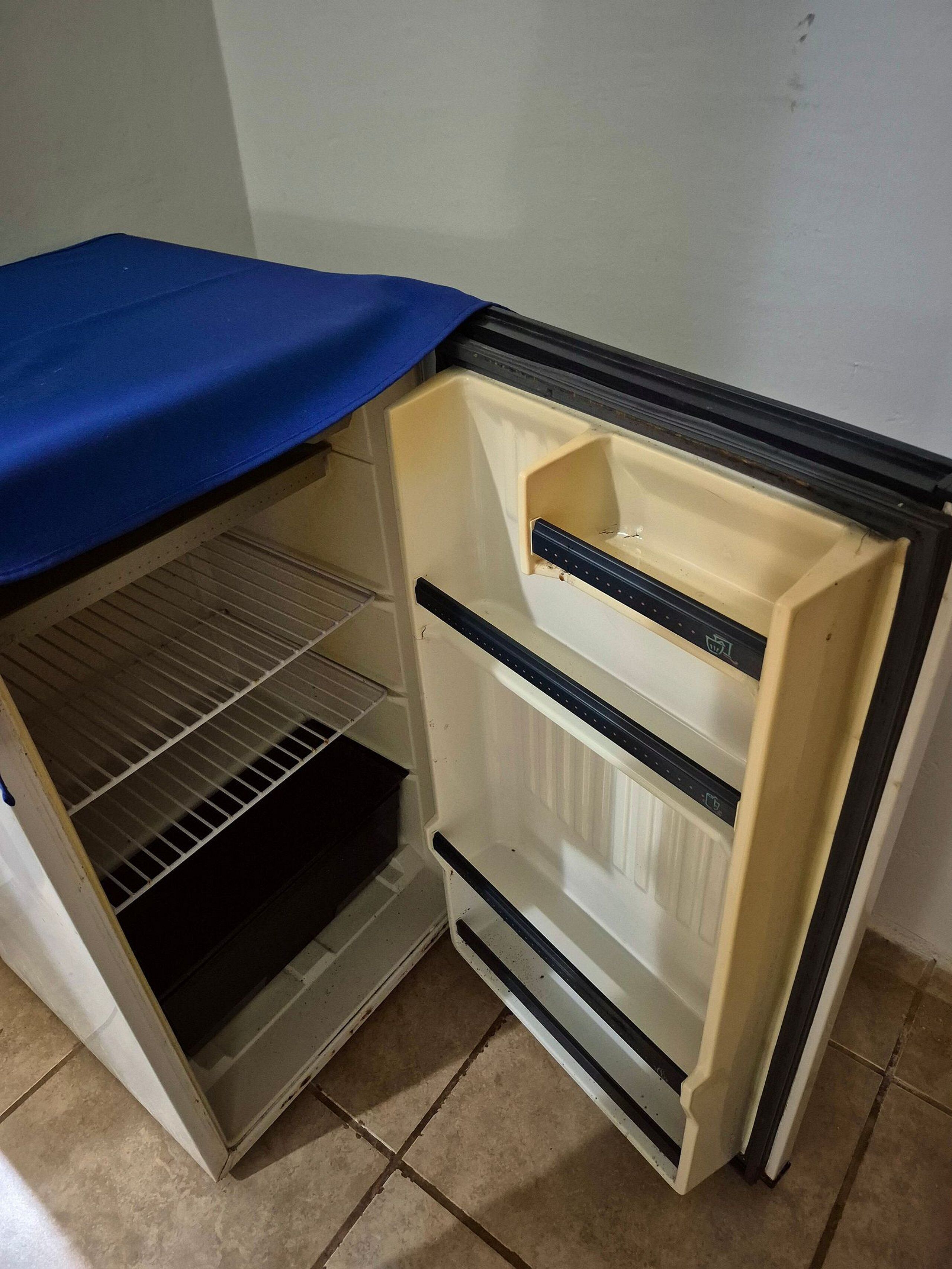 A compact refrigerator with a blue cover, a freezer compartment, and a shelf.