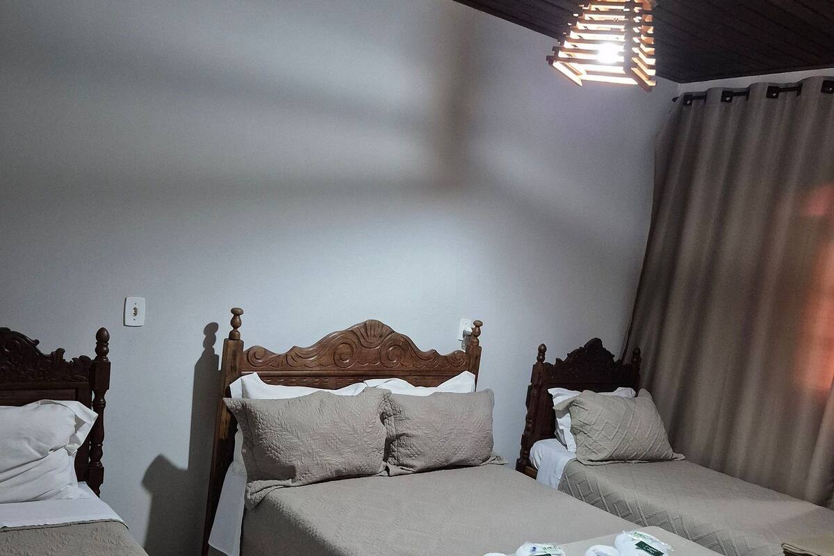A hotel room with two beds, wooden headboards, a hanging light fixture, and a curtain.