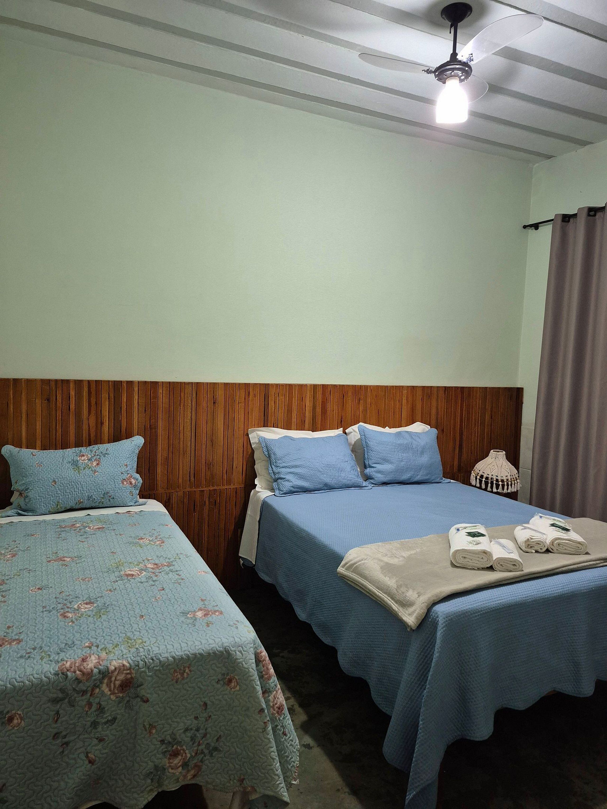 Habitación de hotel con dos camas, cabecera de madera, ventilador de techo y una mesita de noche con lámpara.
