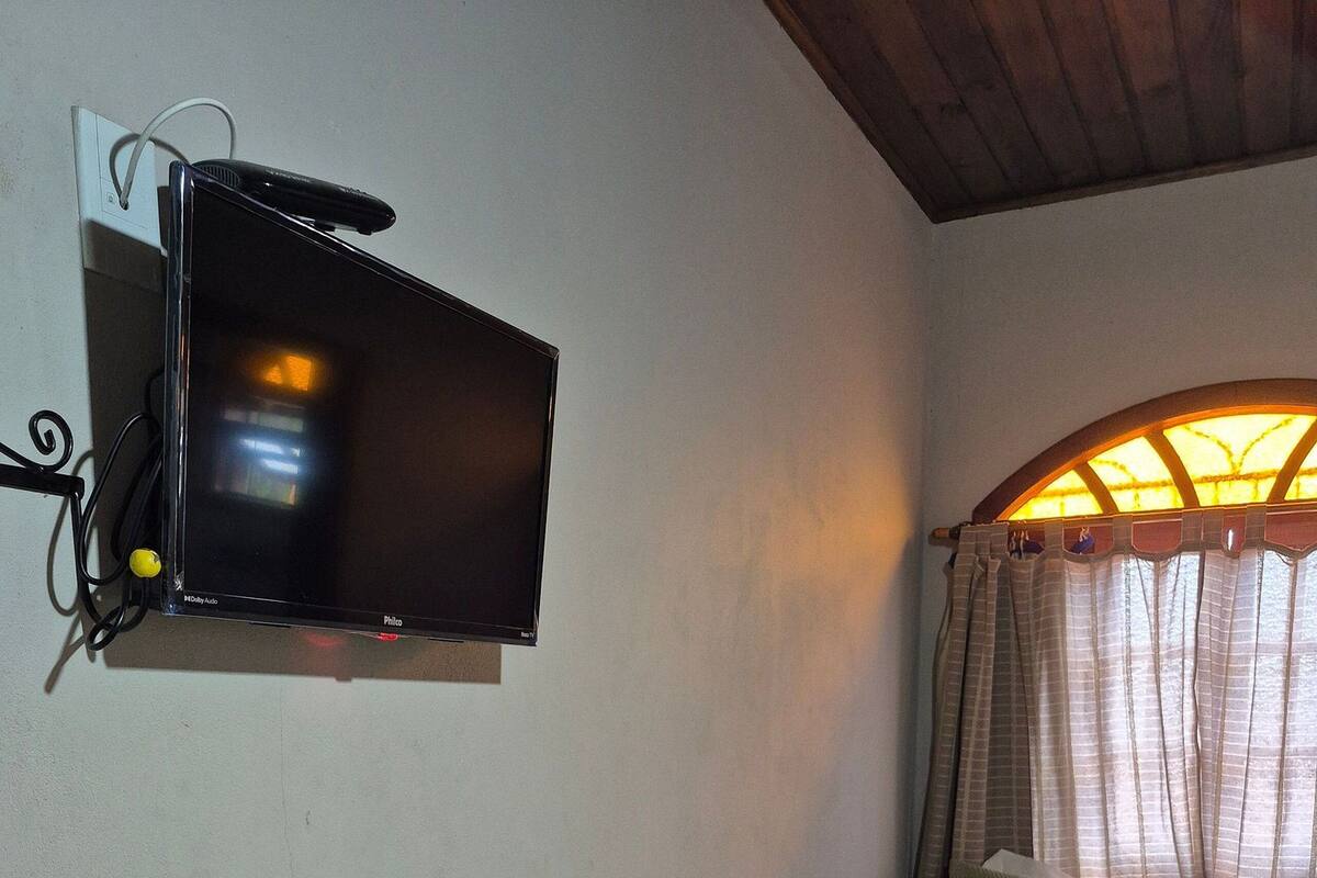 A single bed with a green bedspread, a pillow, and a folded towel. A flat-screen TV is mounted on the wall above the bed.