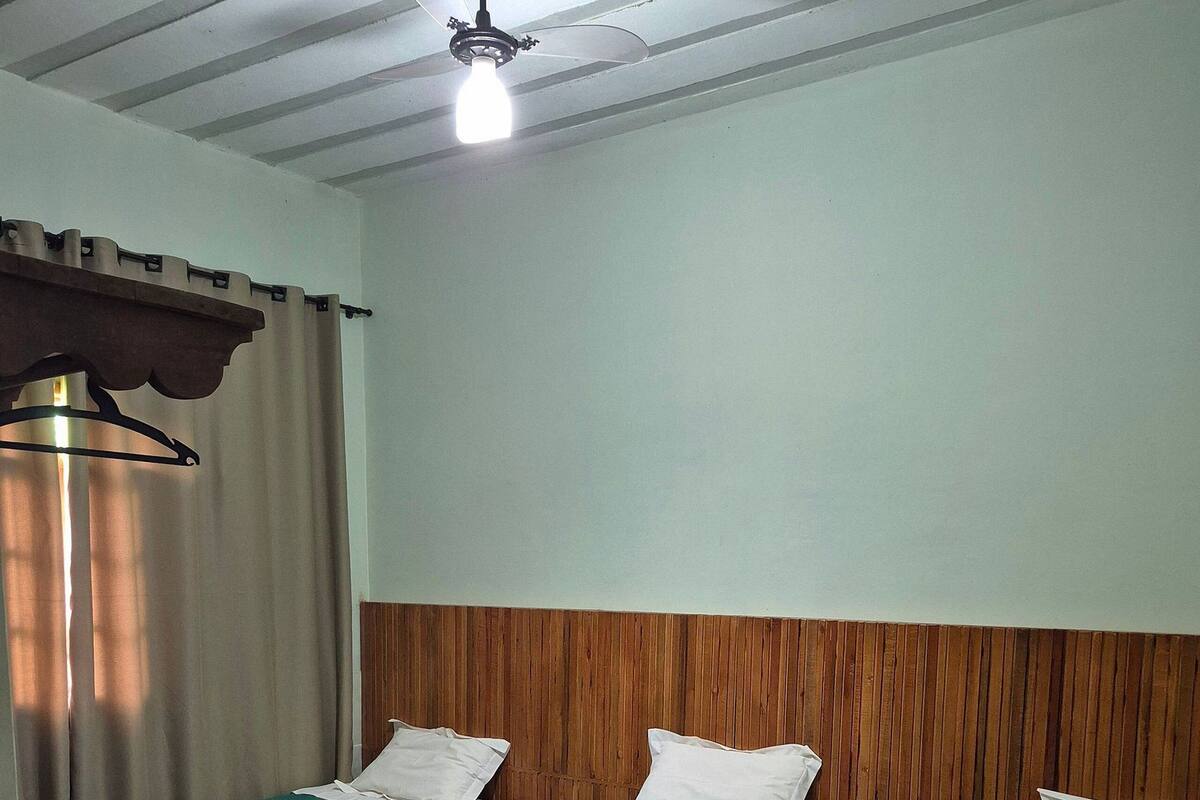 A room with two beds, a wooden headboard, a ceiling fan, and a table with a lamp.