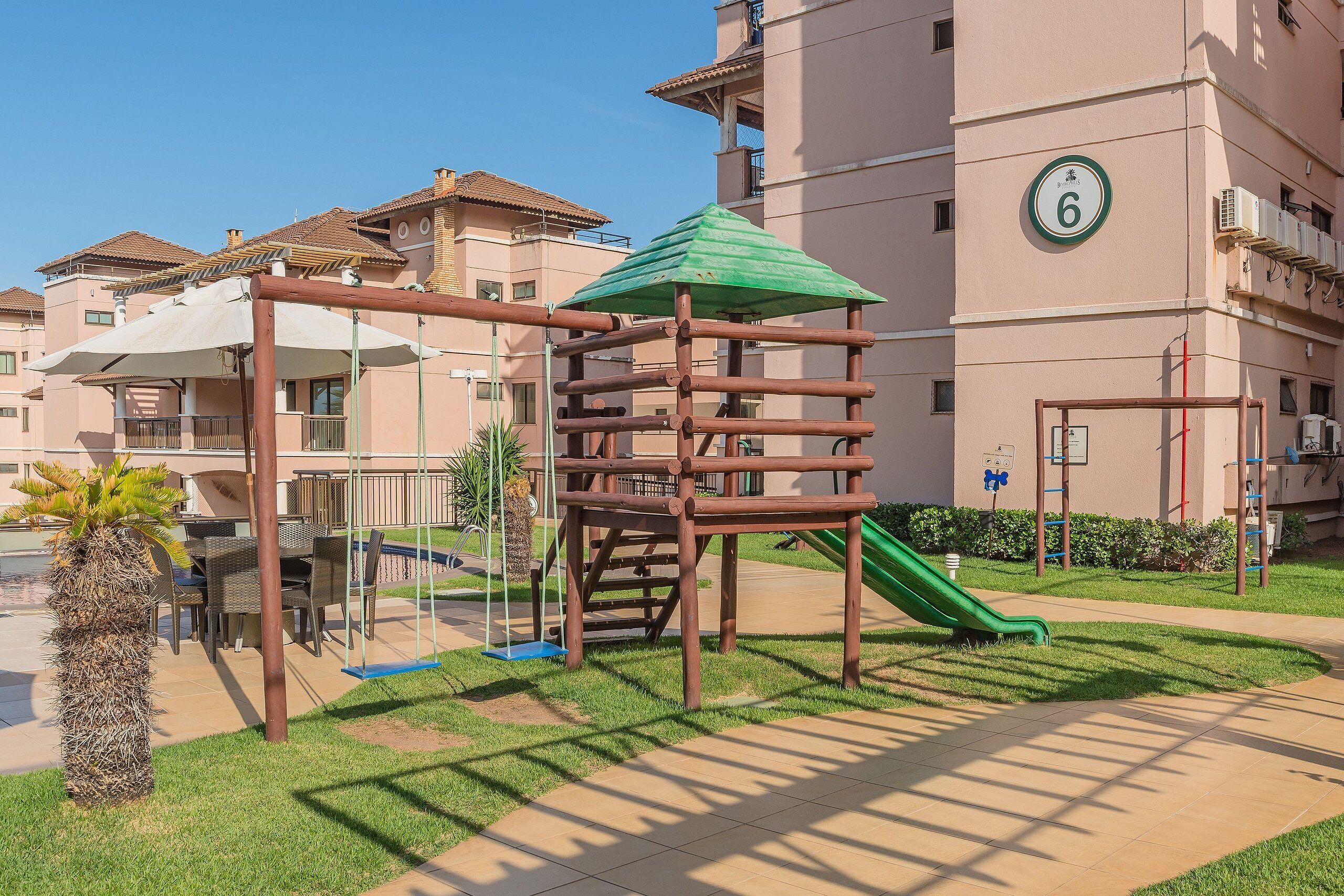 Un patio de recreo con tobogán y estructura para escalar, rodeado por un edificio con balcones y un cartel con el número 6.