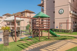 Ein Spielplatz mit Rutsche und Klettergerüst, umgeben von einem Gebäude mit Balkonen und einem Schild mit der Nummer 6.