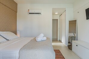 Une chambre d’hôtel comprenant un lit, une armoire, une table de chevet, un climatiseur fixé au mur et une porte donnant sur une autre pièce.