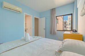 Ein Hotelzimmer mit Bett, Fenster mit Blick, Klimaanlage und einem kleinen Tisch mit Handtuch und Flasche.