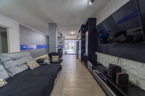 Ein modernes Wohnzimmer mit einer Couch, einem an der Wand befestigten Fernseher und einer Küche im Hintergrund.