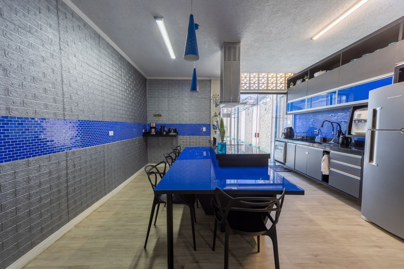 A modern kitchen with a blue-tiled backsplash, stainless steel appliances, and a dining area with a blue table and chairs.