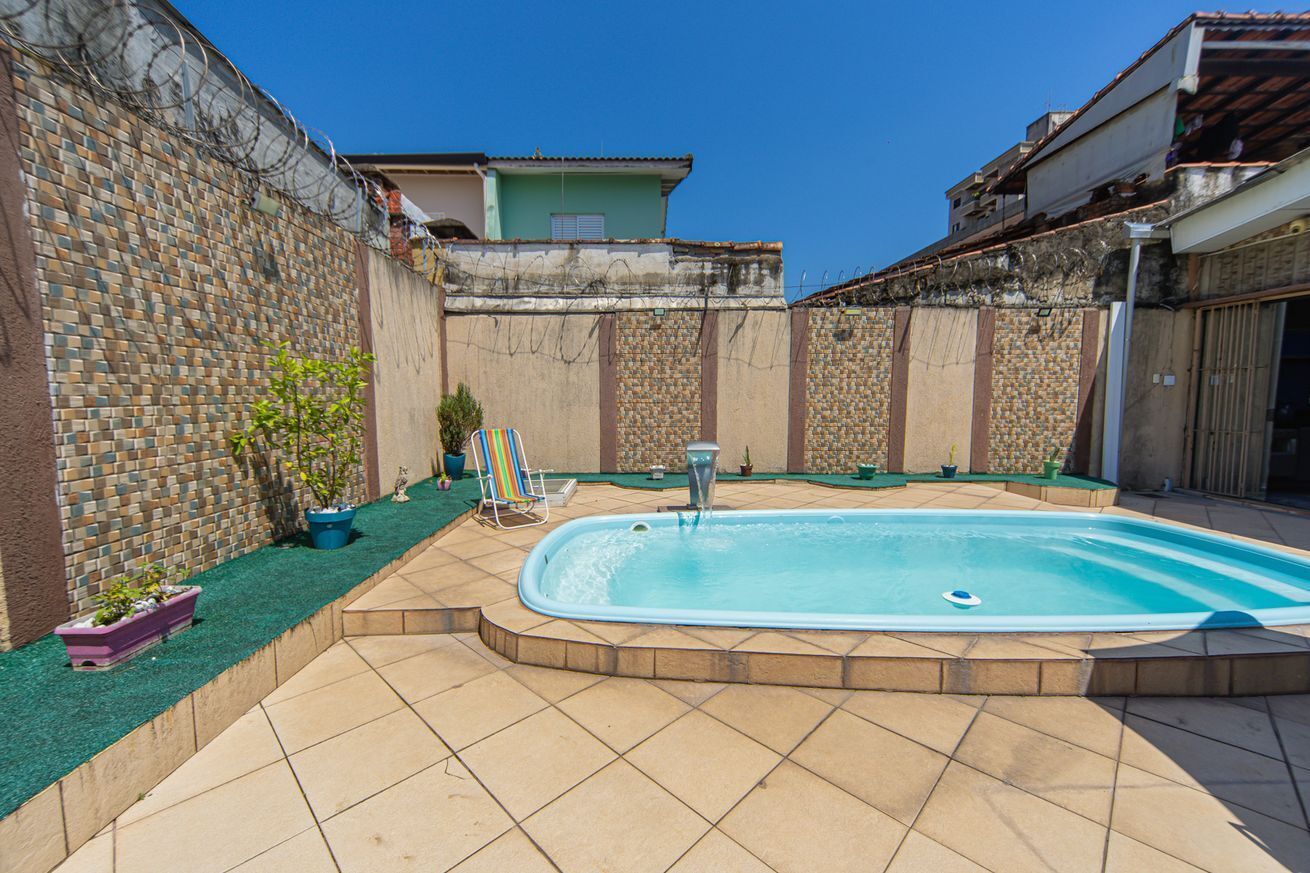 Una piscina con borde de baldosas, rodeada por un muro de ladrillo y un pequeño jardín con plantas en macetas.