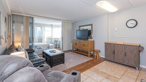 Un salon moderne avec un canapé, un téléviseur, un meuble en bois et une grande fenêtre.