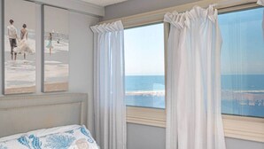 Une chambre avec vue sur l’océan, un lit recouvert d’une couvre-lit à motifs bleus et blancs, et deux tableaux encadrés accrochés au mur.