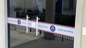 Entrada con puerta de vidrio y barrera de seguridad, con vista despejada al exterior y un edificio de diseño moderno.