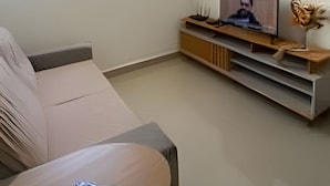 Ett vardagsrum med en soffa, ett soffbord, en tv på ett träställ och ett stort fönster.