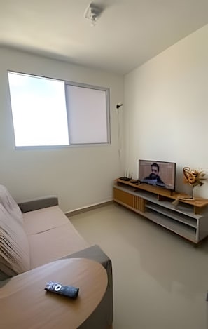 A living room with a sofa, a coffee table, a TV on a wooden stand, and a large window. - 1403 Apto 2 Qtos Cabedelo João Pessoa (Cabedelo)