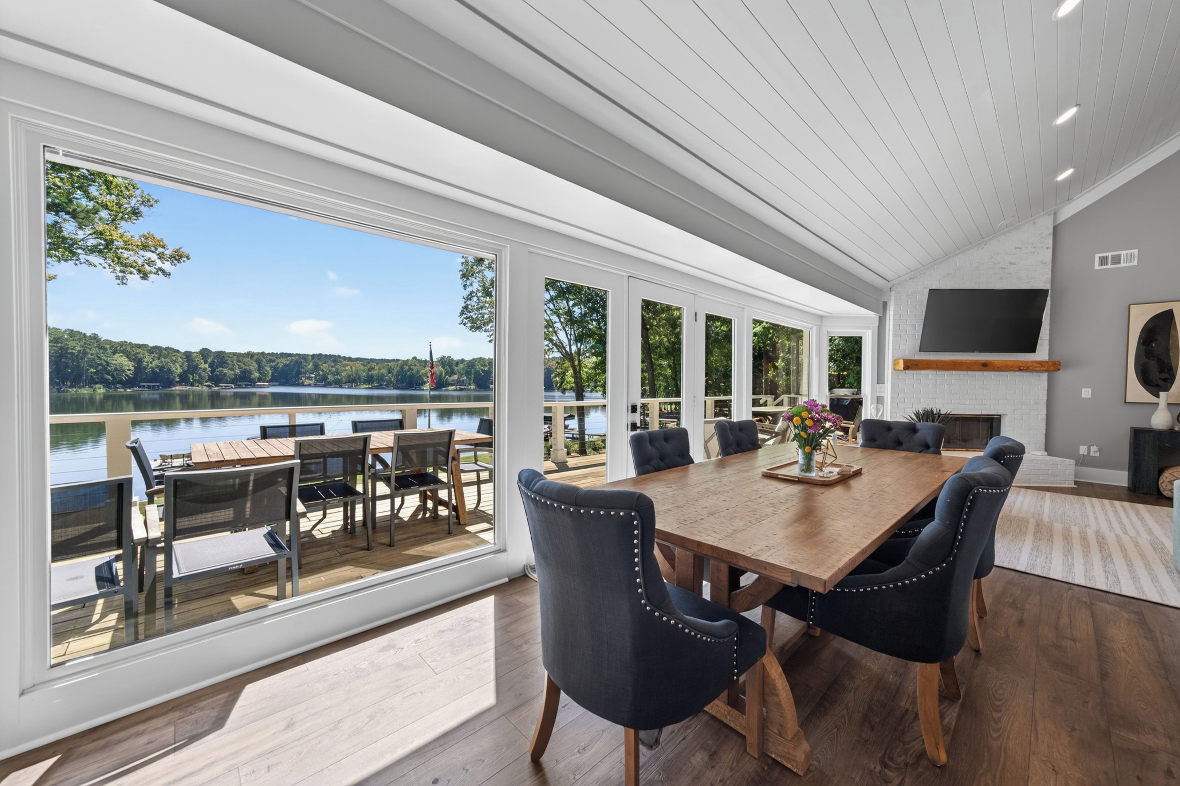 A spacious dining area with a large wooden table and modern chairs, overlooking a lake.