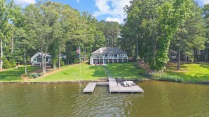 A house with a dock extending into a lake, surrounded by trees. - Lakefront Retreat | Lake Oconee | Boat & Jet Skis (Eatonton)