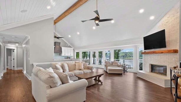 A spacious living room with a fireplace, a television mounted on the wall, and a ceiling fan. - Lakefront Retreat | Lake Oconee | Boat & Jet Skis (Eatonton)