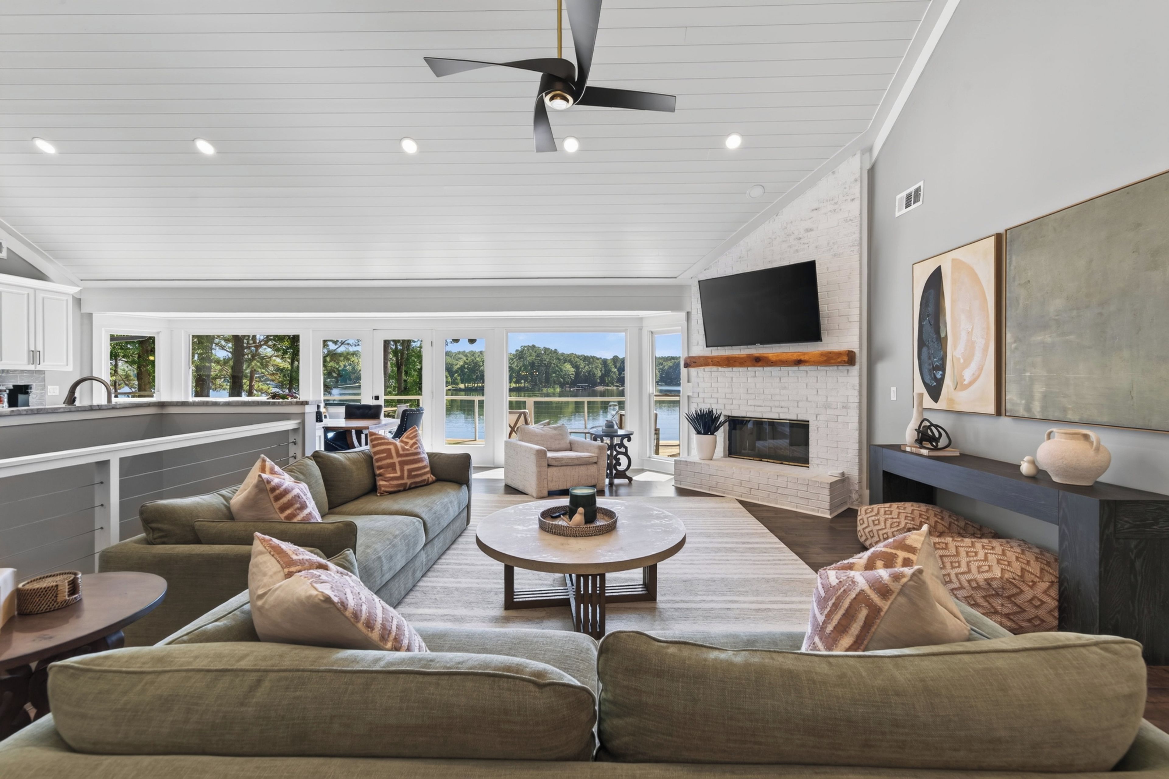 A spacious living area with a fireplace, a large TV mounted on the wall, and a view of the outdoors through the windows.