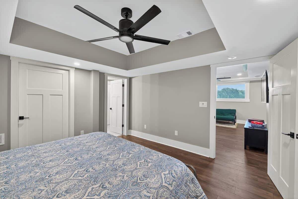 A bedroom with a bed, a ceiling fan, a door, and a view of another room.