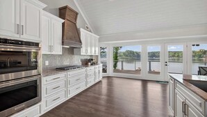 A spacious kitchen with white cabinetry, a large island, and a view of a lake through glass doors. - Lakefront Retreat | Lake Oconee | Boat & Jet Skis (Eatonton)