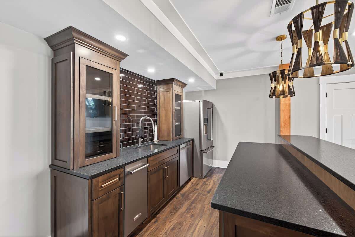 A modern kitchen with dark wood cabinets, a black countertop, and a unique chandelier.