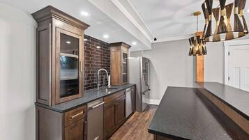 A modern kitchen with dark wood cabinets, a black countertop, and a unique chandelier.