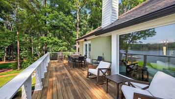 A deck with outdoor furniture, a glass balustrade, and a view of a lake.