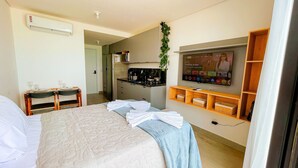 Ett hotellrum med en säng, ett skrivbord med en stol, ett litet kök och en tv som är monterad på väggen.