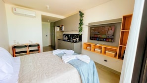 A hotel room with a bed, a desk with a chair, a kitchenette, and a TV mounted on the wall. - OCEAN - FLAT STUDIO FRENTE MAR (João Pessoa)