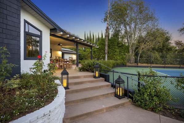 A residential property with a covered outdoor seating area, steps leading to a pool, and a well-maintained garden.