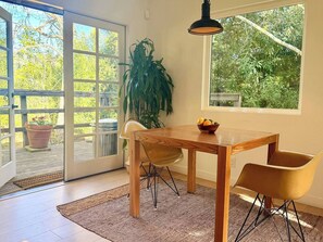 Un coin repas avec une table en bois, deux chaises, une plante en pot et une fenêtre donnant sur un paysage verdoyant.