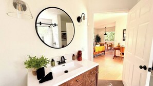 A bathroom with a wooden vanity, a round mirror, and a white sink. - Charming Private Cottage in Ojai (Ojai)