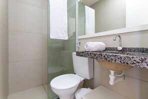 A bathroom with a toilet, a sink with a granite countertop, a mirror above the sink, and a glass shower enclosure. - Beach Townhouses 4 - Duplex in Porto das Dunas by Carpediem (Aquiraz)