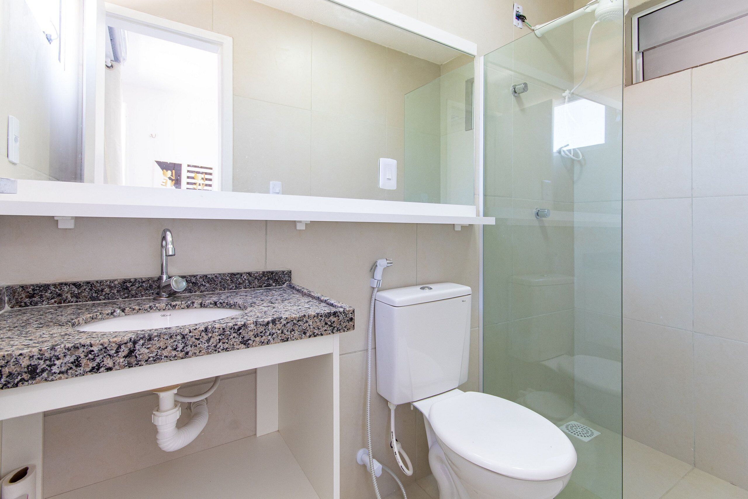 Baño con lavamanos de encimera de granito, inodoro, cabina de ducha de vidrio y espejo sobre el lavamanos.