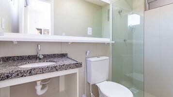 Baño con lavamanos de encimera de granito, inodoro, cabina de ducha de vidrio y espejo sobre el lavamanos.