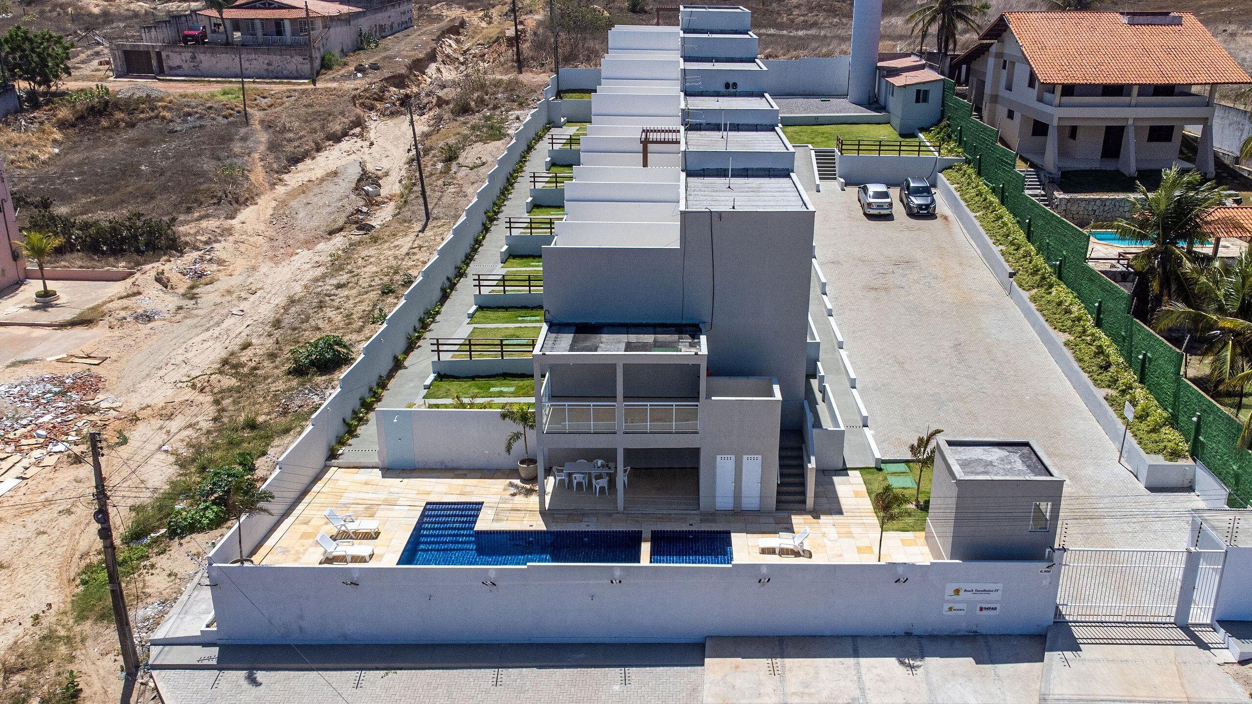 Un edificio moderno con piscina en la azotea, varios balcones y una cerca verde.